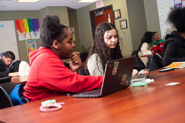 Students working together on laptops at a table in a classroom.