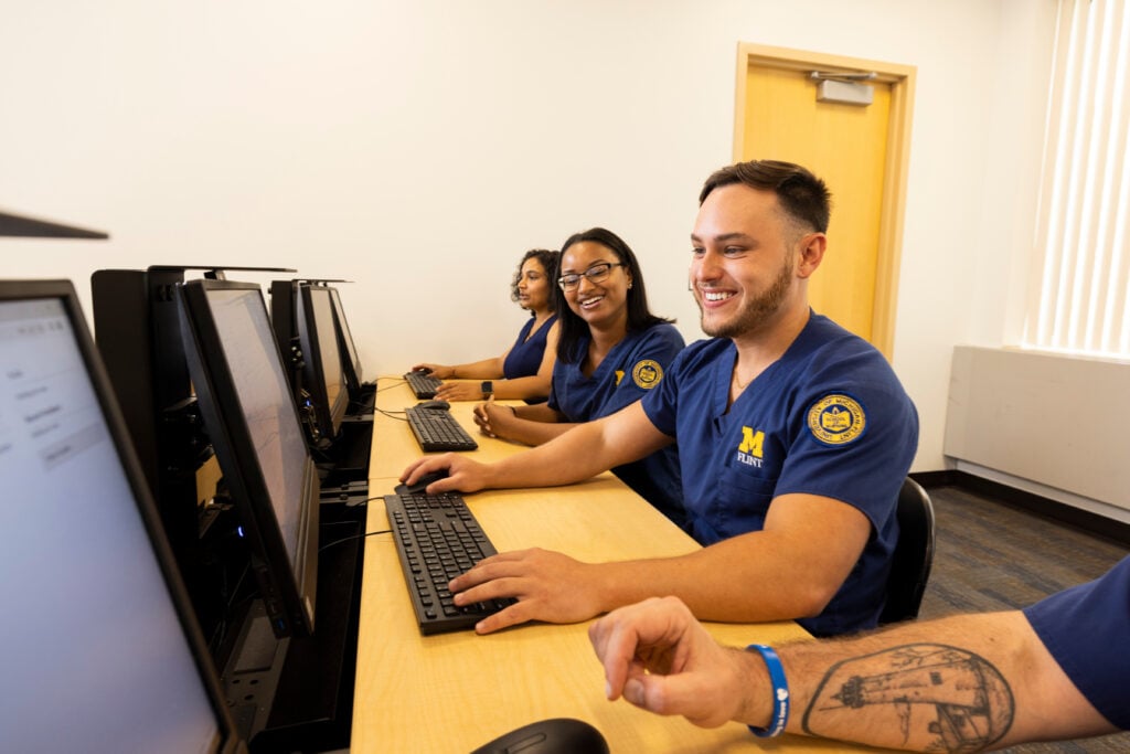 A group of four people in blue scrubs are sitting at computers, smiling and engaged in a collaborative activity.