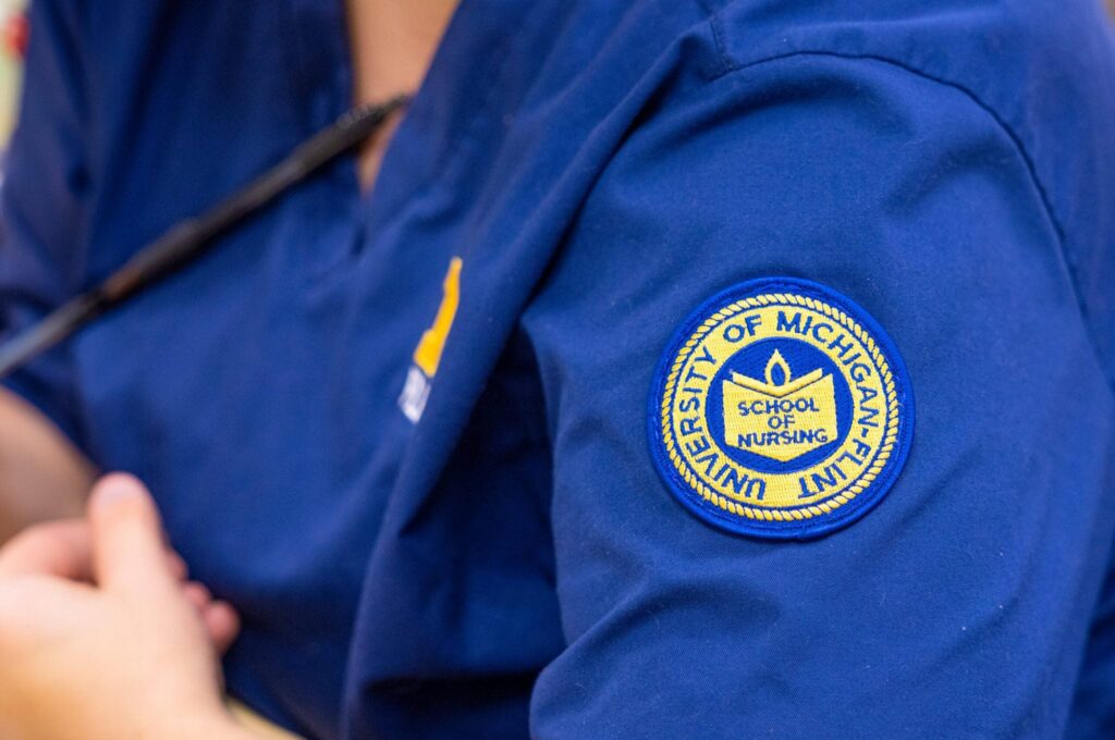 A close-up of a blue shirt sleeve featuring a circular patch that reads "University of Michigan School of Nursing."
