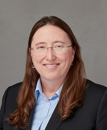 Portrait of a woman with brown hair and glasses in a dark blazer and blue top