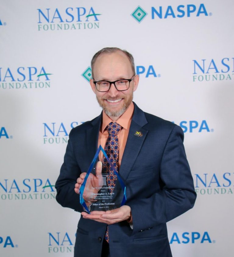 A man holding an award in front of a background of logos for NASPA Foundation