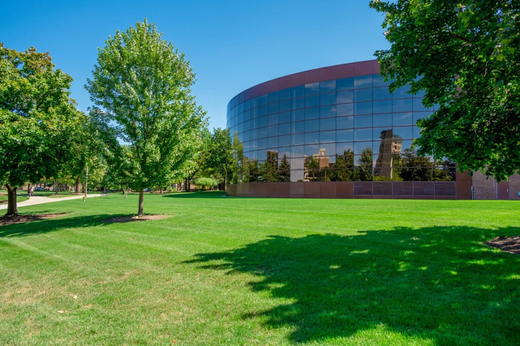 A curved building with lots of windows in sunlight and green grass