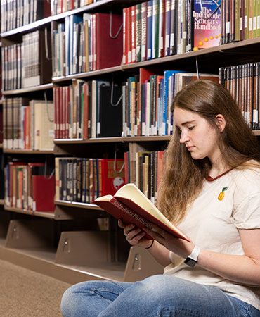 Female student sitting on the library floor reading a book