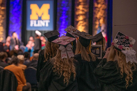 Group of graduates in cap and gowns looking at the stage