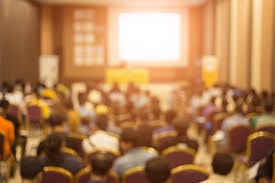 BLurry room of people sitting in front of a presentation