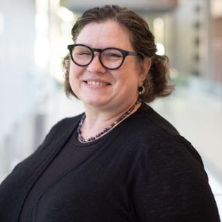 Amalie Helms smiling and wearing glasses, standing in a well-lit indoor space.