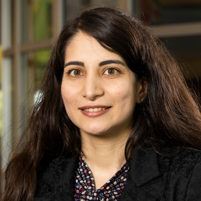 Azadeh Sadeghi with long dark hair smiles in a professional setting, wearing a black jacket and a patterned shirt.