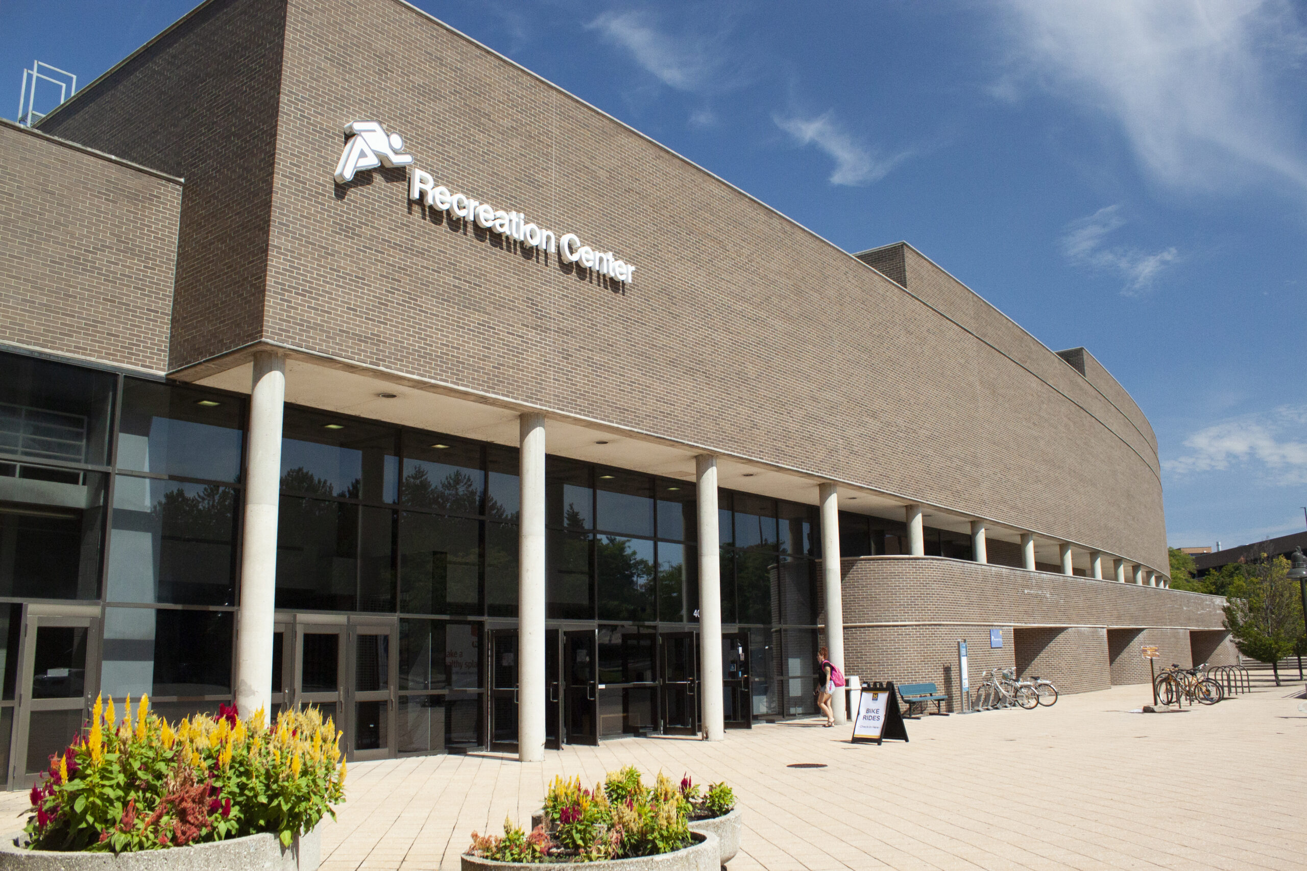 A brick building with a sign reading "Recreation Center," featuring large glass doors and flower planters in front.