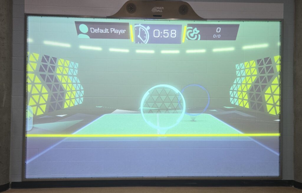 A digital game interface displayed on a wall, showing a timer, player name, and two circular targets in a colorful environment.