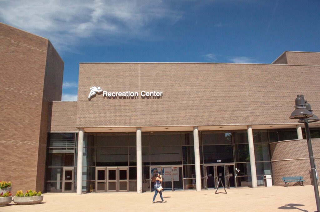 A person walks in front of a modern building with a sign that reads "Recreation Center."