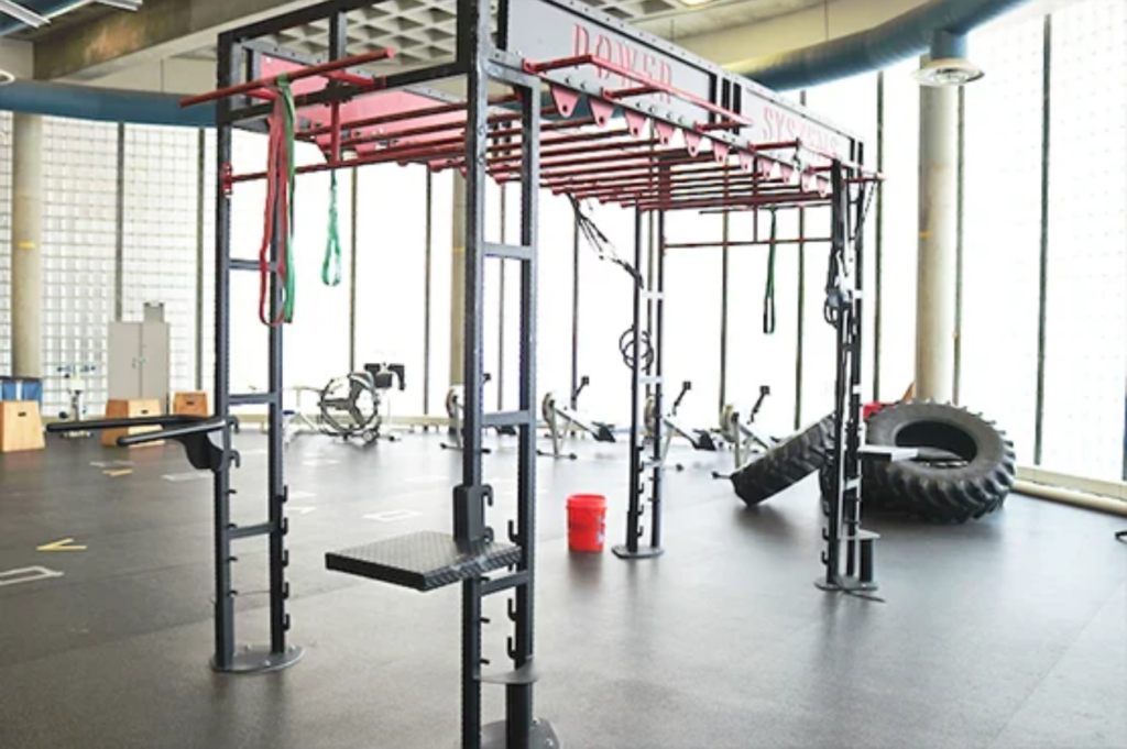 A gym area featuring a power rack with resistance bands, a large tire, and exercise equipment in a well-lit space.