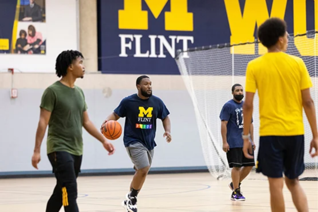 A group of four people playing basketball in a gym, with one person dribbling a ball and others positioned nearby.