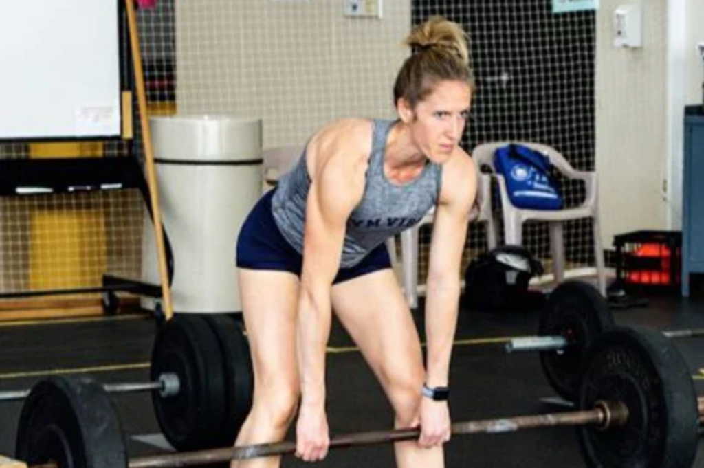 A person is preparing to lift a barbell in a gym setting, focusing intently on the weight.