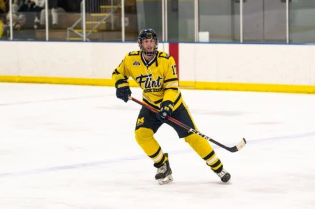 A person in a yellow hockey uniform skates on the ice, holding a hockey stick and looking towards the puck.