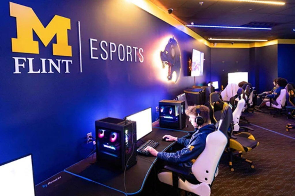 A gaming room with multiple computers and chairs, featuring a wall sign that reads "M FLINT | ESPORTS."