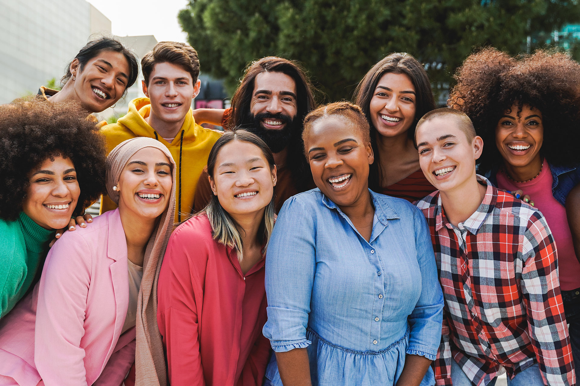 A group of diverse people posing closely together outdoors, smiling at the camera.