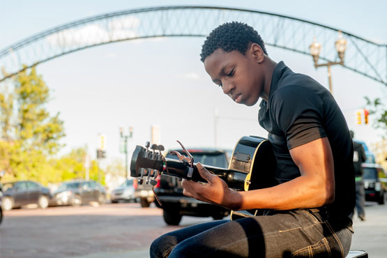 Student playing guitar on Saginaw Street.