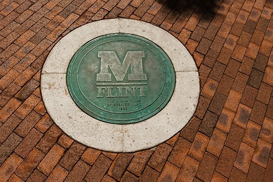 A bronze University of Michigan-Flint medallion embedded in a brick paver walkway.