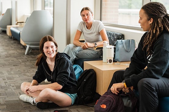 Three students sitting and chatting together in a campus lounge area.