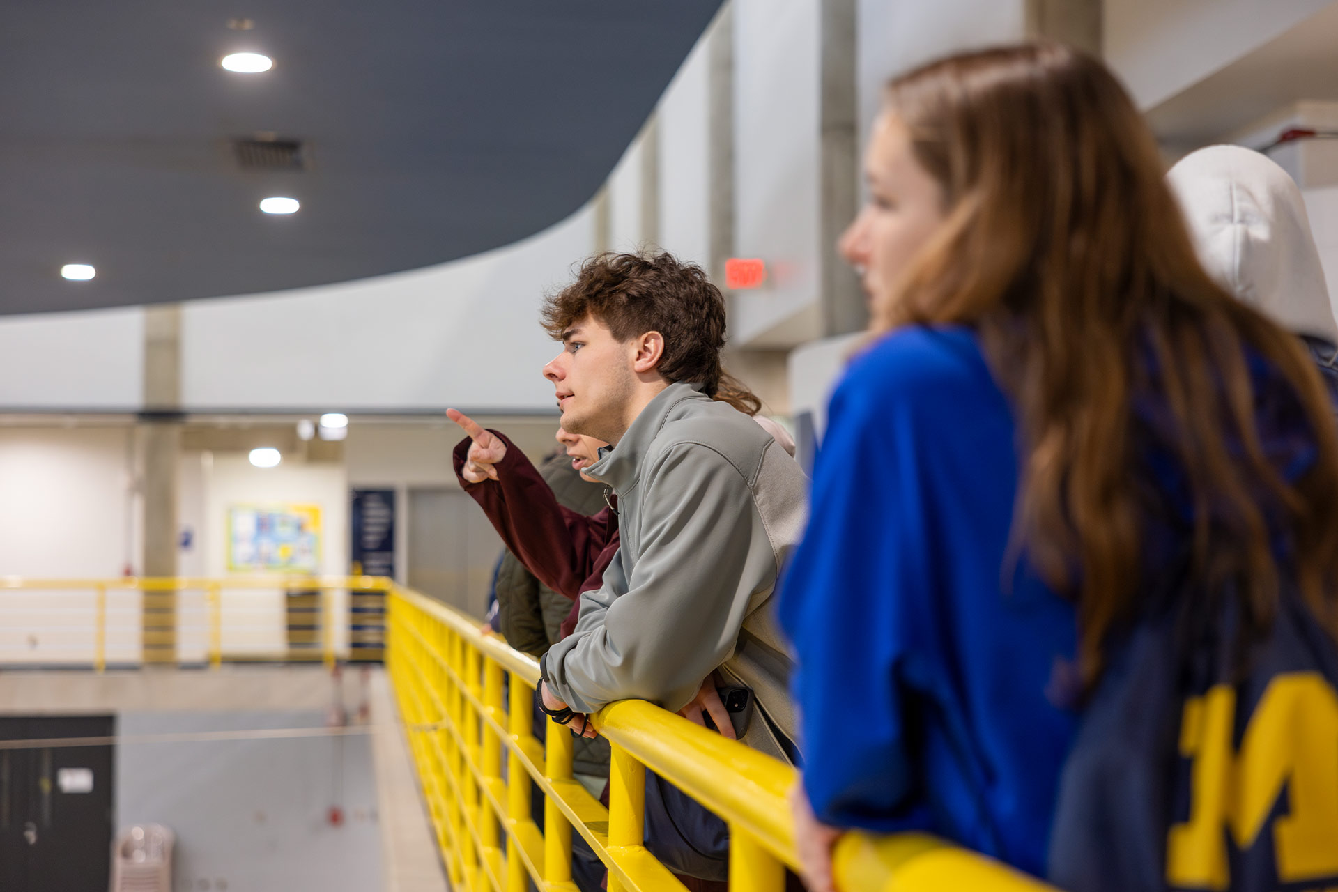 A group of people stands by a yellow railing, with one person pointing and speaking while others listen.