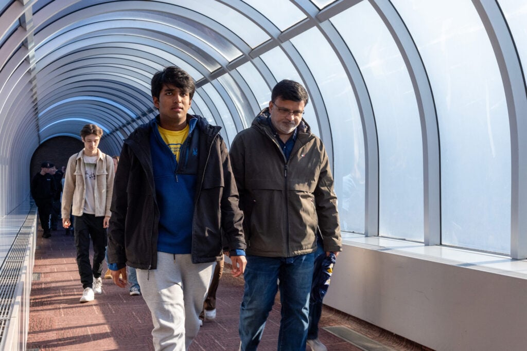 A group of people walking through a brightly lit, curved glass corridor.