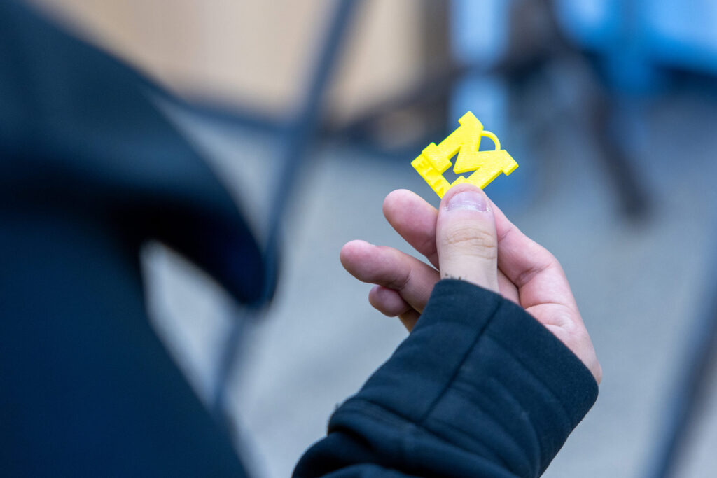 A person holds a yellow plastic letter "M" in their hand, wearing a black jacket.