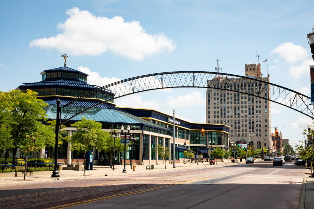 A street view featuring a modern building with a curved archway overhead and a tall historic building in the background.