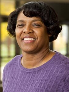 Brenda Harrison smiles while wearing a purple knit sweater. Her short black hair is slightly curled about her ears and forehead.