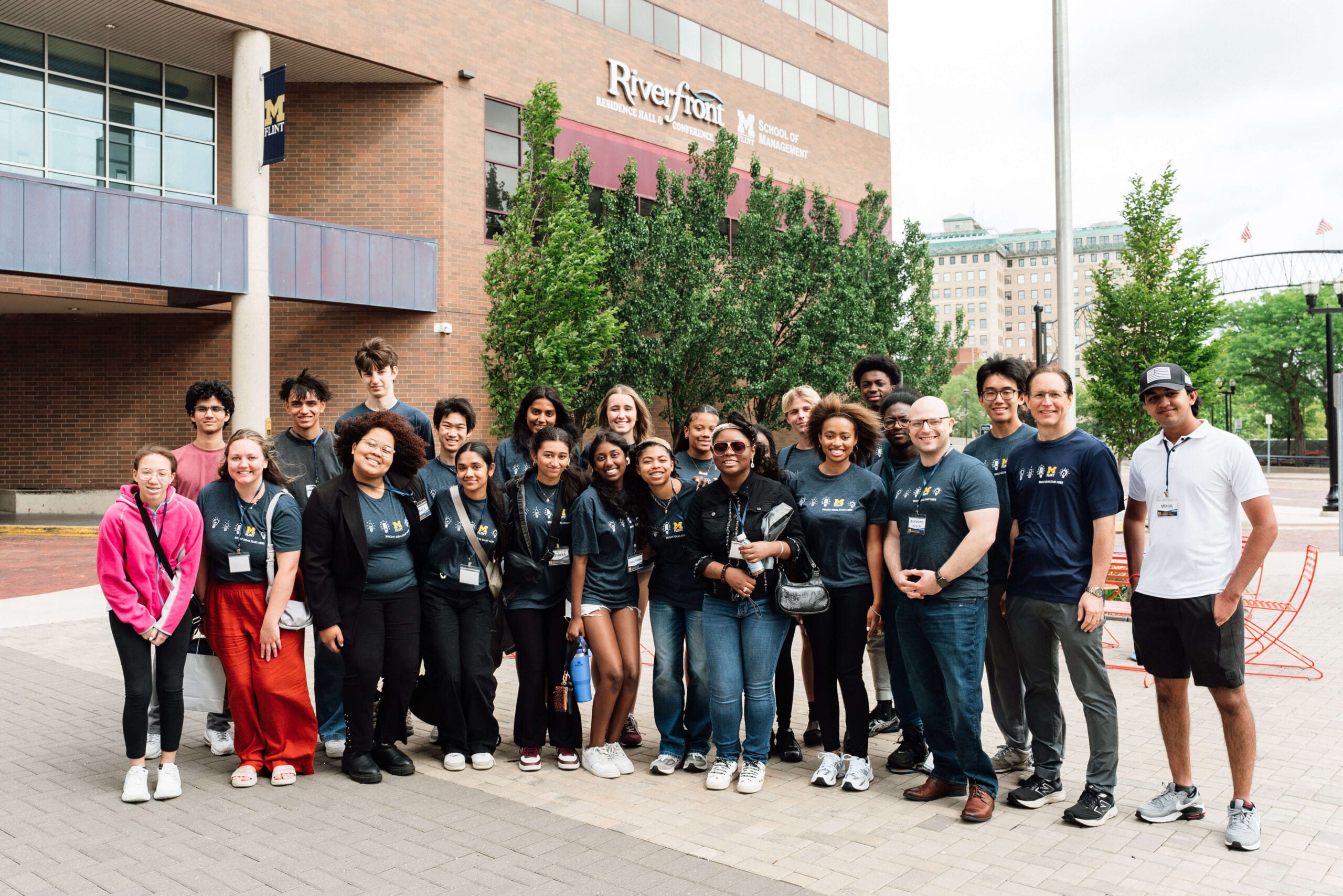 A group of diverse people pose together outside the Riverfront Center, smiling and wearing matching t-shirts.