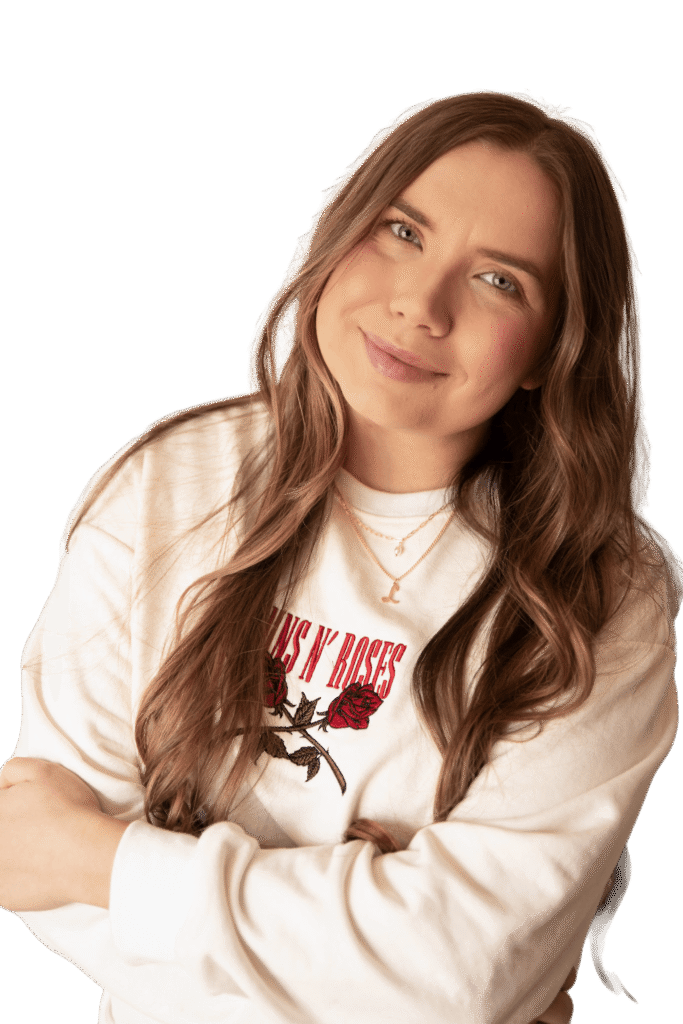 A young woman with long hair smiles while crossing her arms. She is wearing a white sweatshirt with a red graphic design that includes roses.