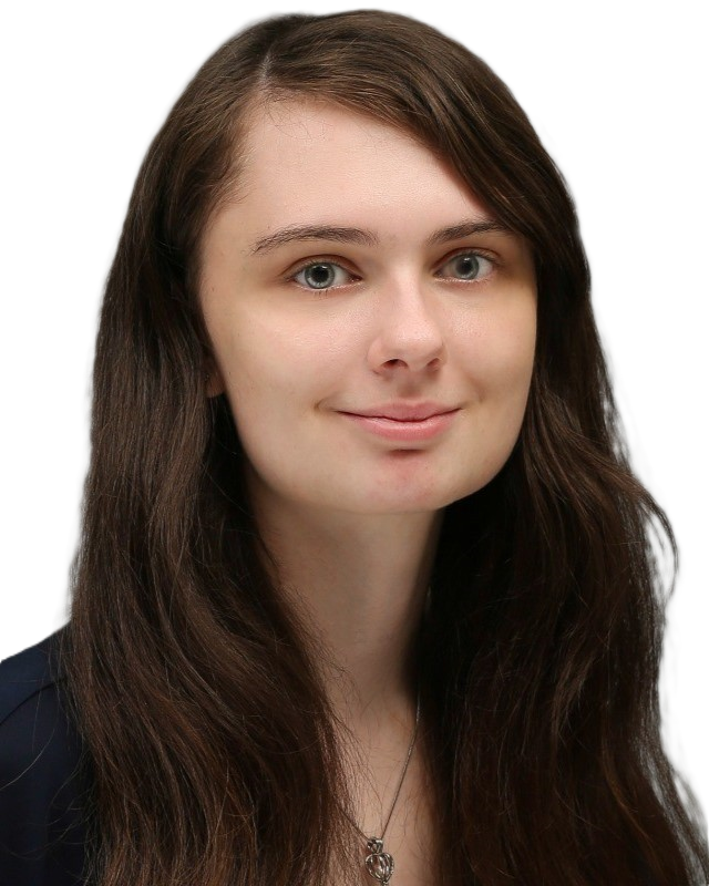 A young woman with long brown hair is smiling for a portrait. She is wearing a navy-blue shirt and a silver necklace with a pendant.