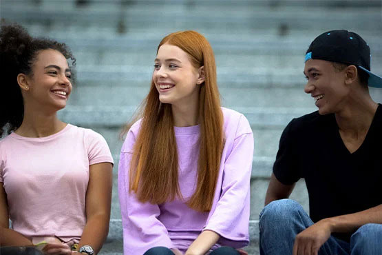 Three people sit on steps, smiling and engaging in conversation.
