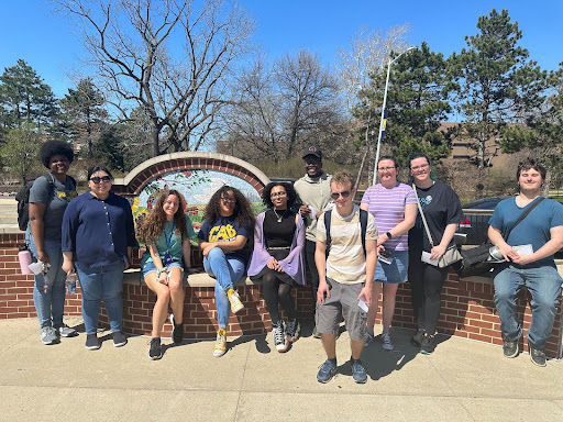 A group of ten people poses together in front of a decorative wall mural on a sunny day.