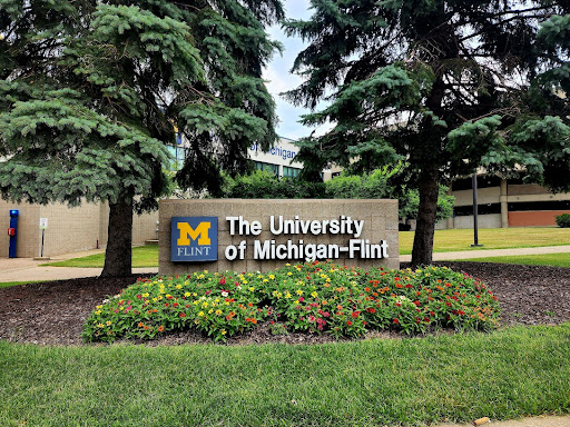 Sign for The University of Michigan-Flint surrounded by greenery and flowers.