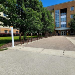 A pathway leading to a building entrance, with bike racks on one side and trees lining the area.