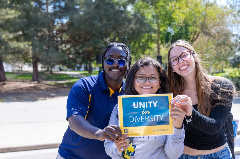 Three people hold a sign that reads "UNITY in DIVERSITY" in a park setting.