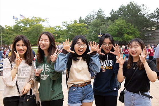 A group of five people poses outdoors, making hand gestures and smiling at the camera.