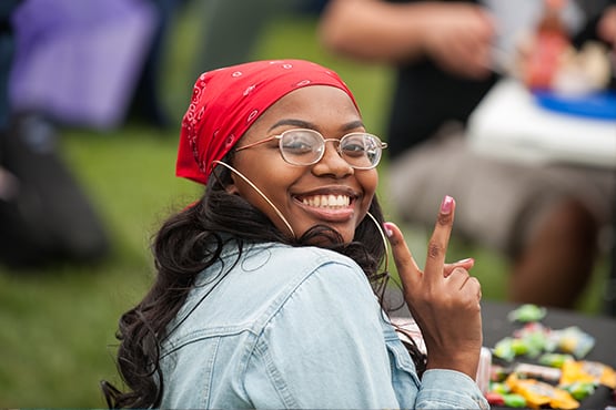A person wearing a red bandana is sitting at a table, making a peace sign with their hand.