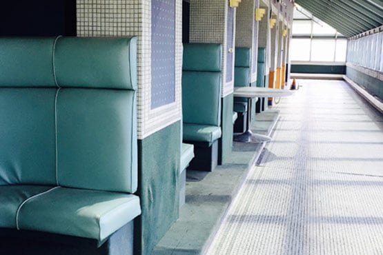 Empty green booth seats lined up along a tiled wall in a sunlit corridor.