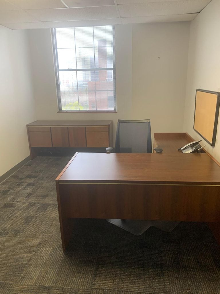 Small office with a wooden desk, office chair, sideboard, window with blinds, and a phone on the desk.