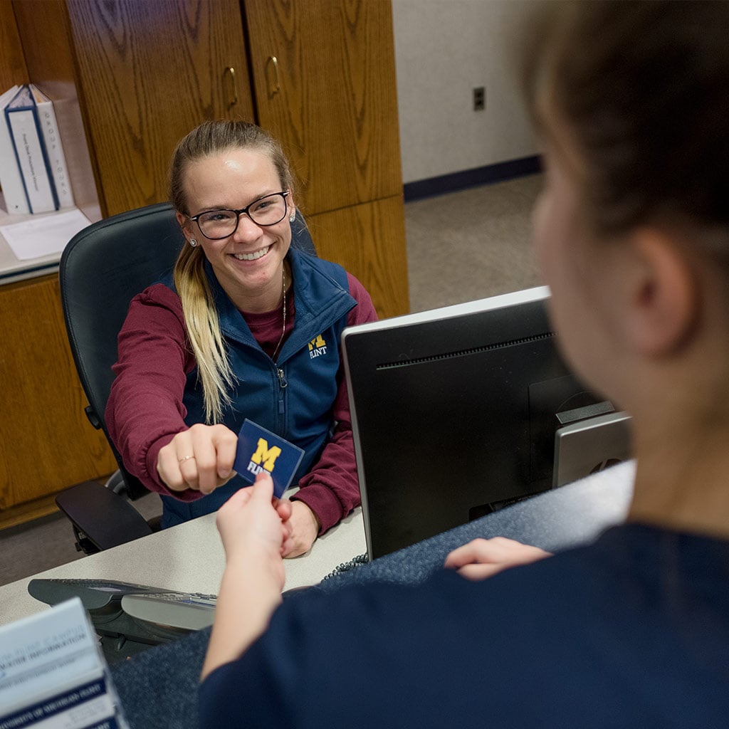 A person at a reception desk hands a card to another person across the counter.