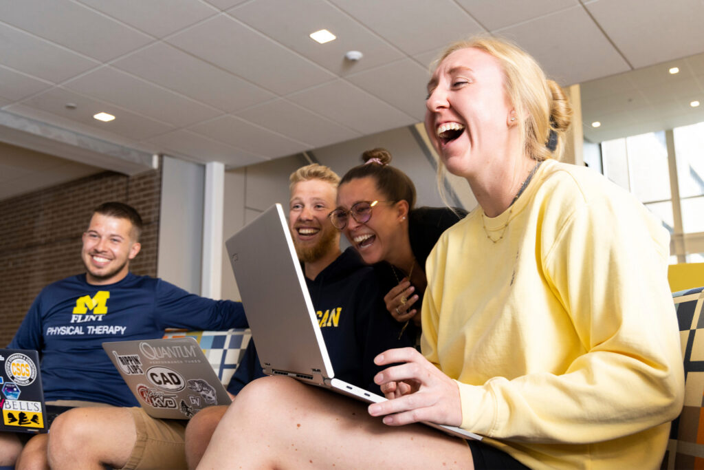 A group of people is gathered together, with one person using a laptop while others lean in to observe.