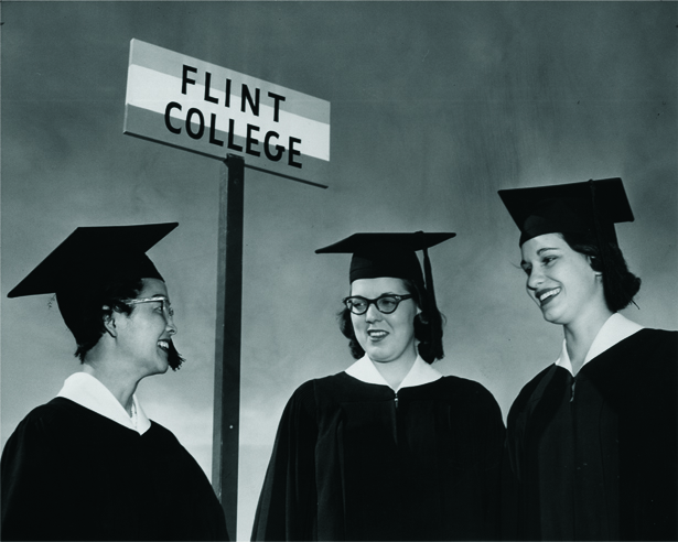 Three graduates in caps and gowns beside a Flint College sign, 1958.