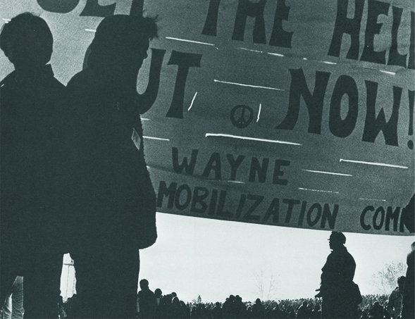 Silhouetted crowd holding protest signs at an anti-Vietnam War demonstration on campus.