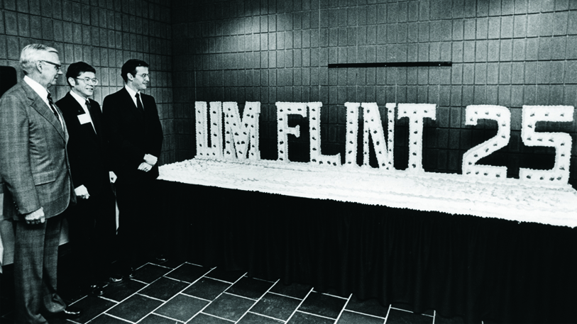 Group photo at a table spelling out ‘UM FLINT 25’ for the university’s 25th anniversary.