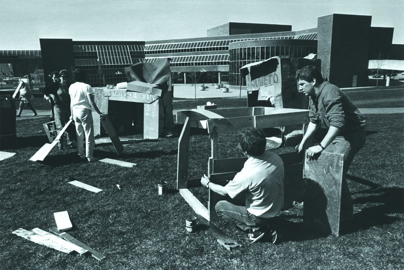 Students assembling a plywood and cardboard ‘shanty town’ structure on the campus lawn.