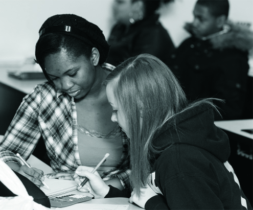 Two students studying together, writing in notebooks.