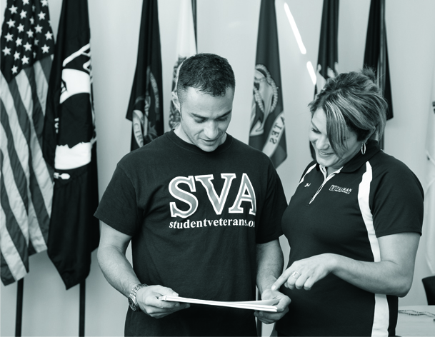 Student veterans standing with an American flag and other flags at the Student Veterans Resource Center opening.