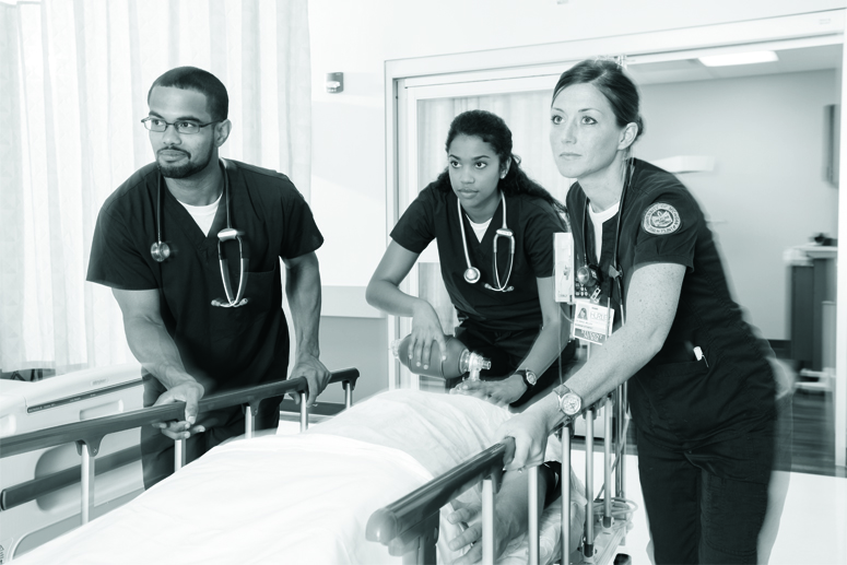 Two nursing or pre-med students assisting a patient in a hospital bed.