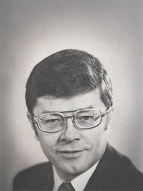 Portrait of Conny Nelson with glasses, smiling slightly against a light background.